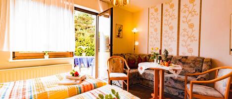Habitación de hotel con dos camas, un sofá, una mesita y vistas a zonas verdes.
