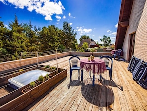 Eine Holzterrasse mit Tisch und Stühlen, umgeben von Backsteinmauern und Blick auf Bäume.