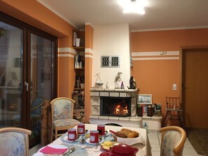 A dining area with a fireplace, a table set for a meal, and a bookshelf with various items.