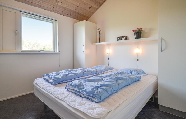 A bedroom with a bed, a window, a shelf with decorative items, and wall-mounted lights. - Stunning home in Knebel with sauna (Knebel)