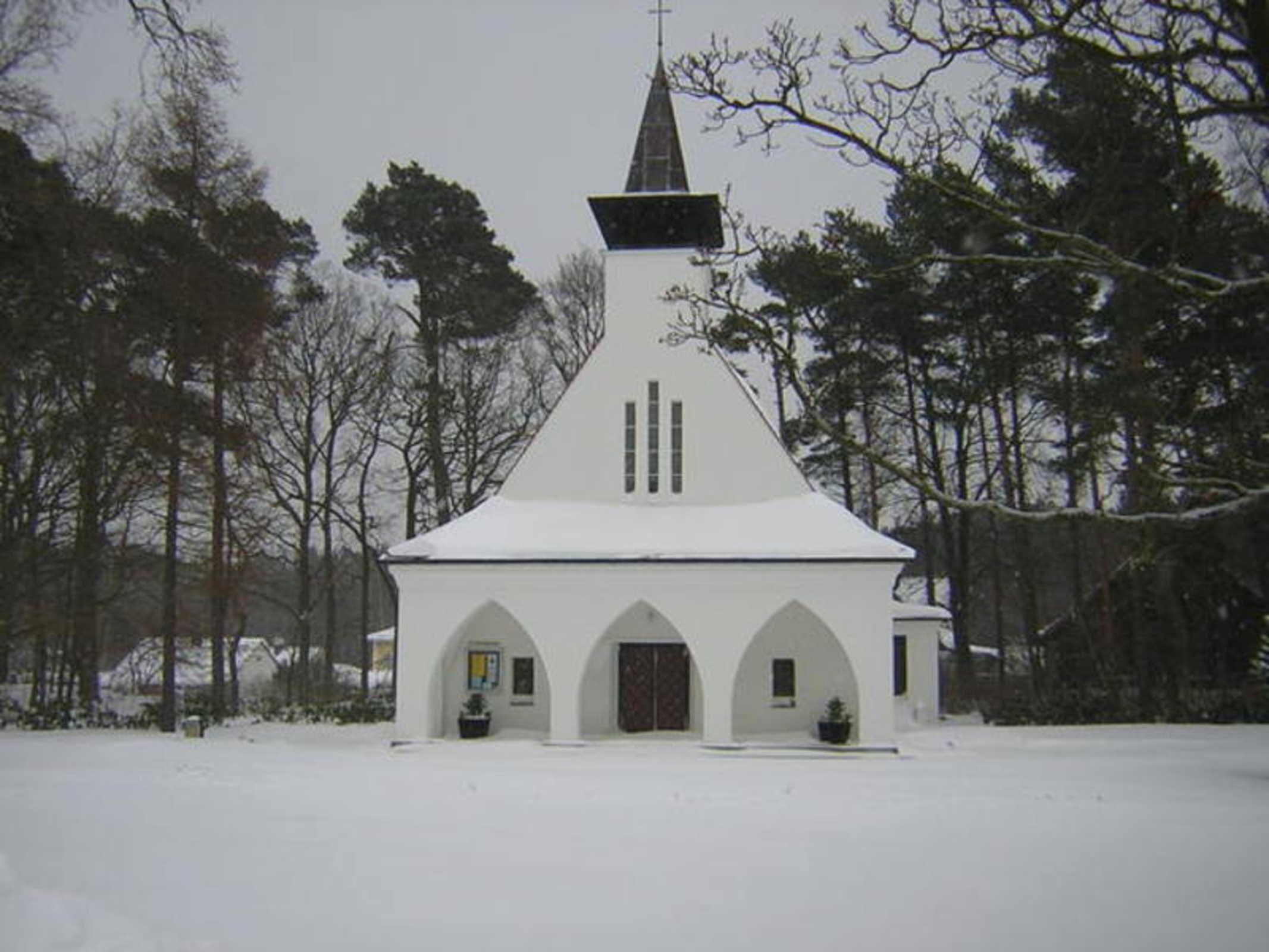 Eine weiße Kirche mit einem Kirchturm und einem Rundbogenportal.