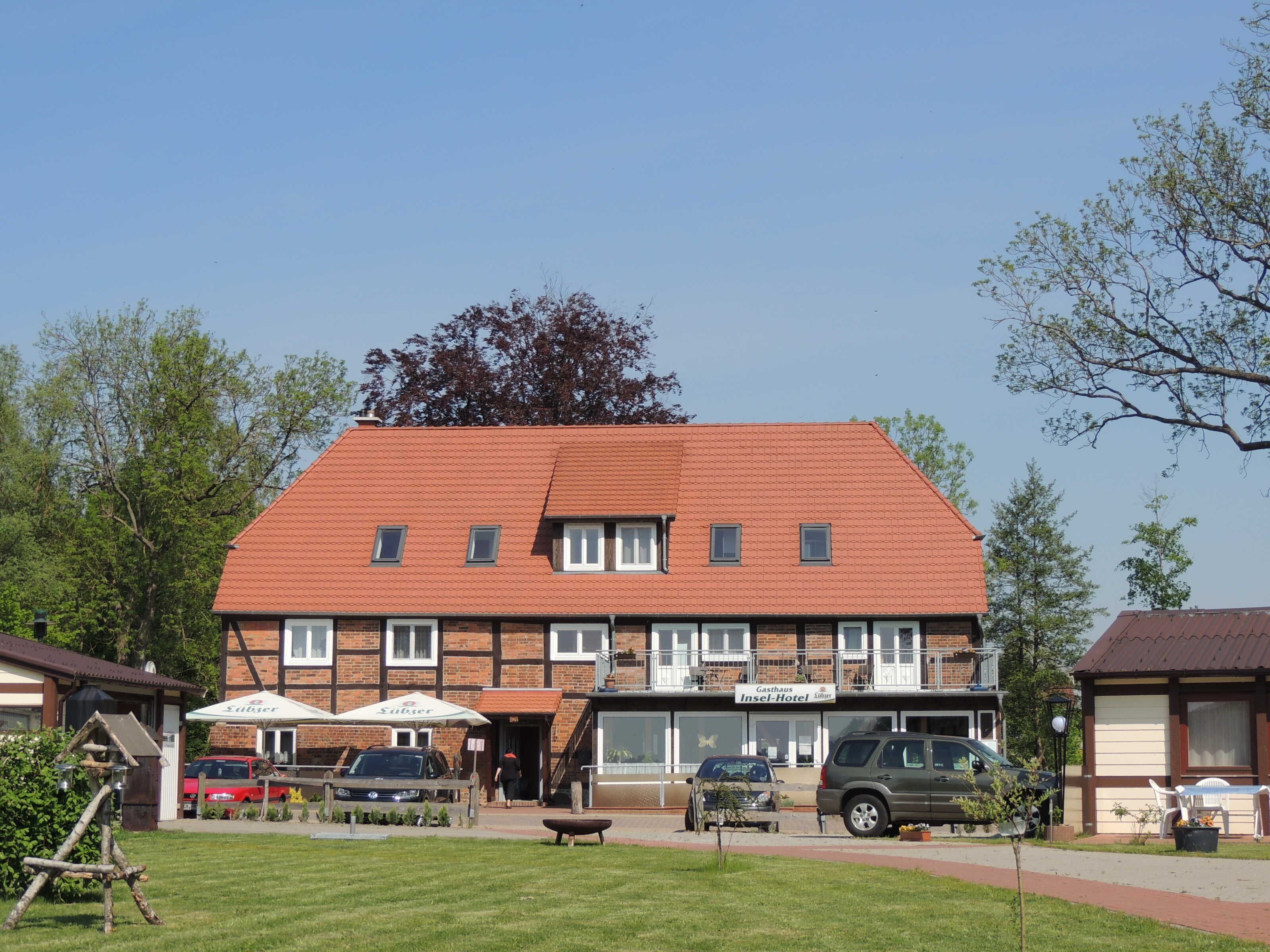 Ein zweistöckiges Gebäude mit rotem Dach, einem Schild mit der Aufschrift 'Gasthaus Insel-Hotel' und mehreren parkenden Autos davor.