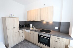 A modern kitchen with light wood cabinets, a black oven, a stainless steel sink, and a built-in stovetop.
