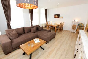 A modern living room with a brown sectional sofa, a wooden coffee table, and a dining area with a wooden table and chairs.