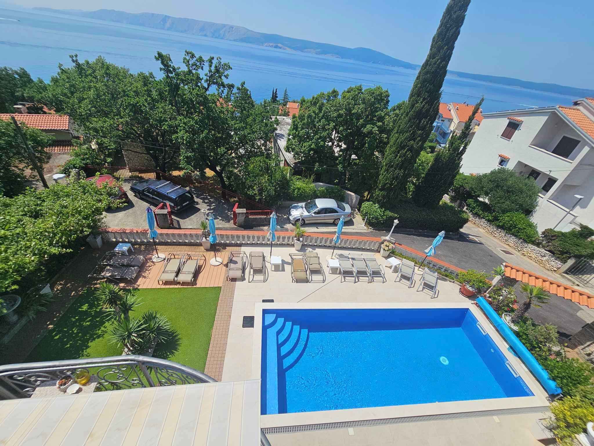 A swimming pool with lounge chairs and umbrellas, surrounded by greenery and buildings.
