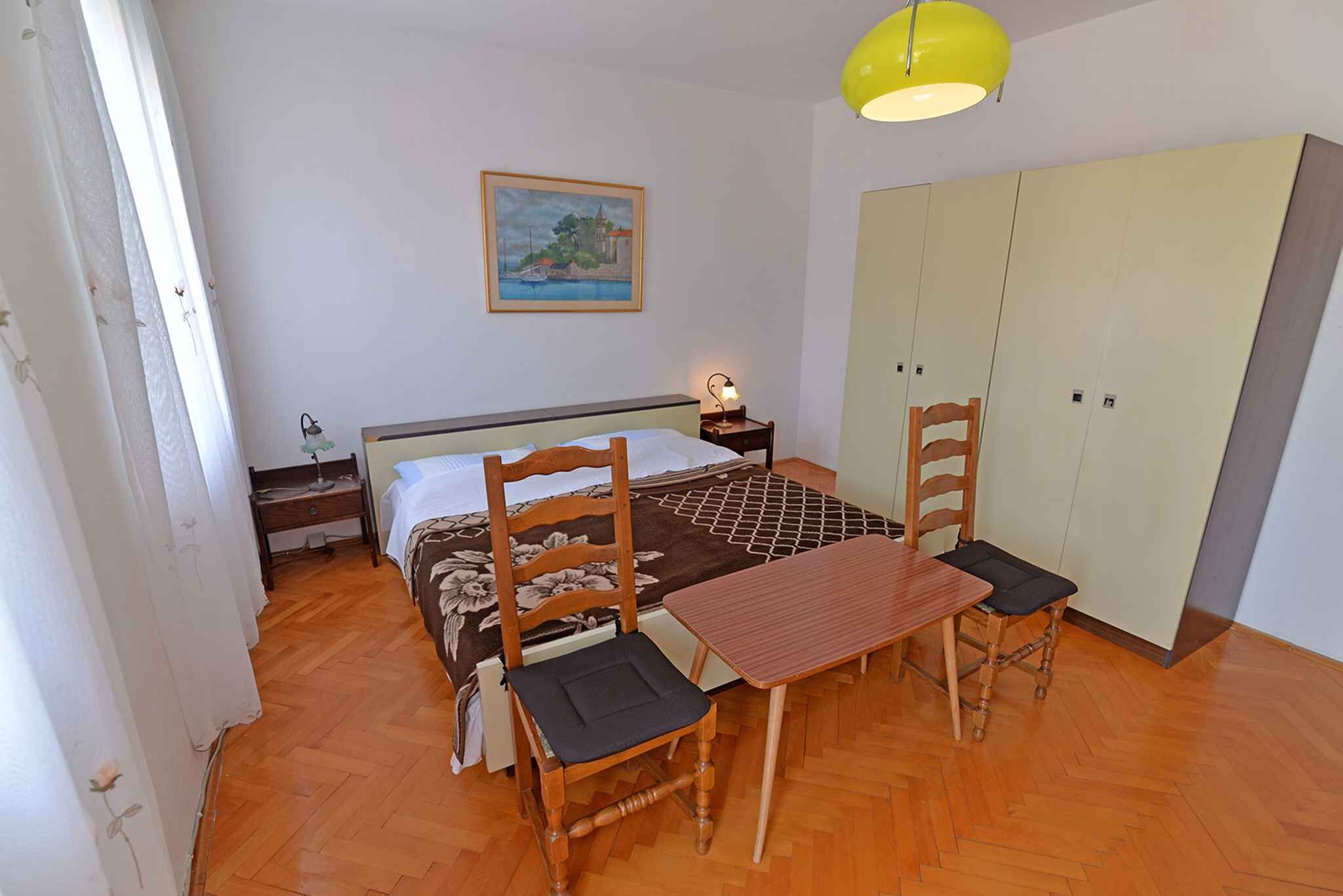 Une chambre à coucher avec un lit, une table en bois, deux chaises, une table de chevet, une lampe, une armoire et un tableau accroché au mur.