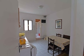 Ein Zimmer mit Esstisch, Stühlen, einem an der Wand befestigten Fernseher, einem Fenster und einer Tür zu einem anderen Raum.