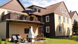 A two-story house with a balcony, outdoor seating, and a chimney.