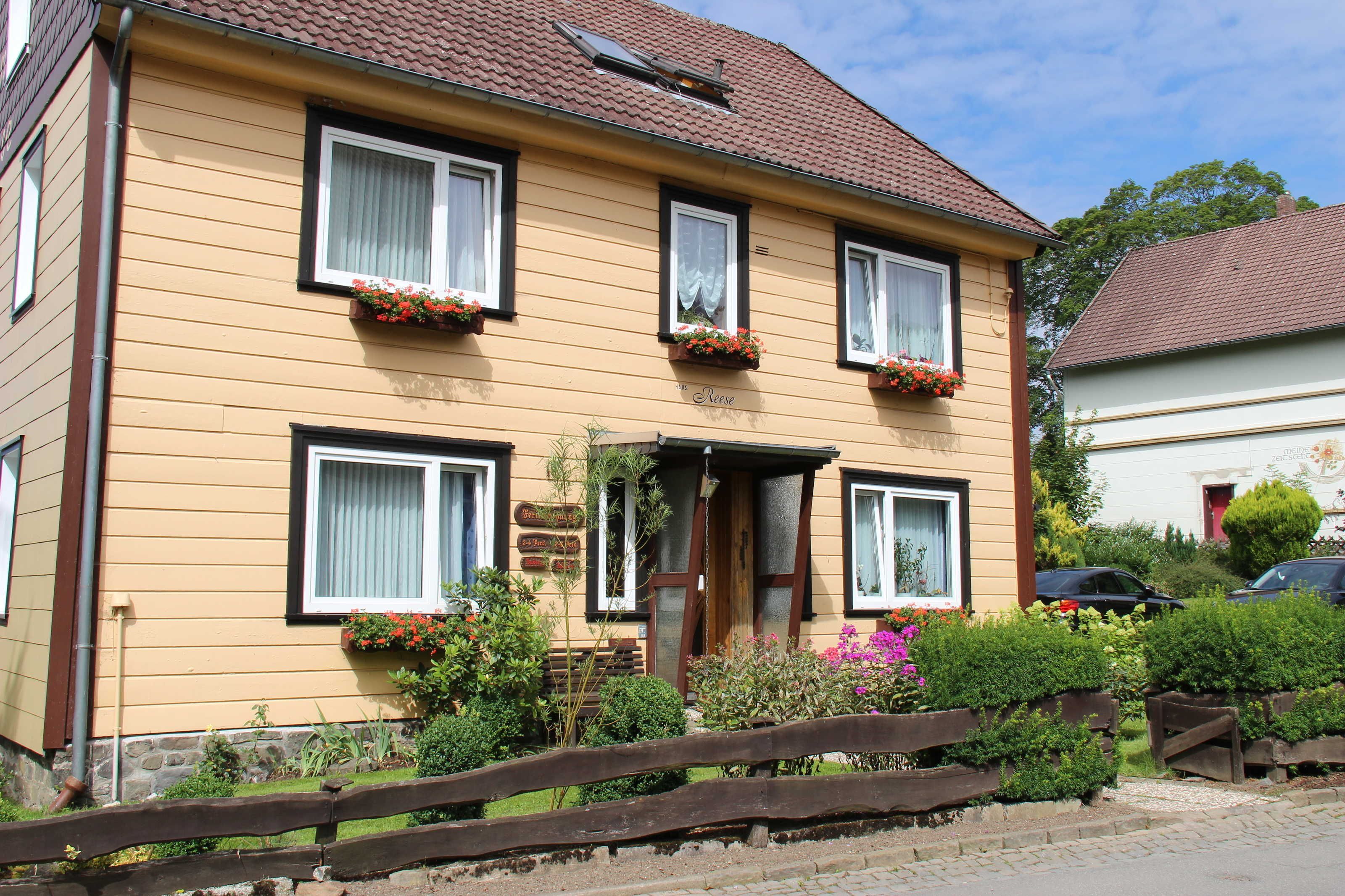 A two-story house with a front entrance, windows with white curtains, and flower boxes on the windowsills.