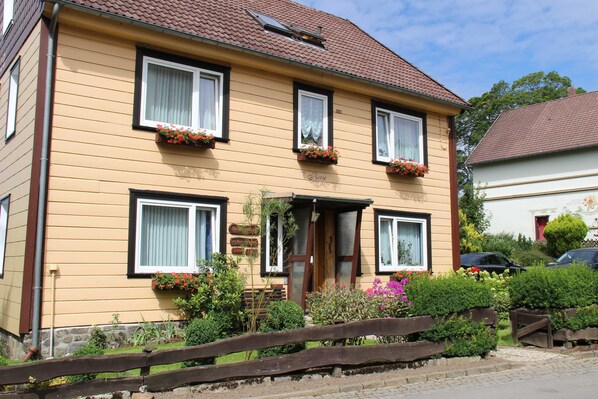A two-story house with a front entrance, windows with white curtains, and flower boxes on the windowsills.
