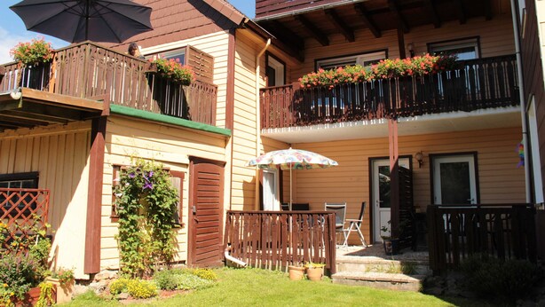 A two-story building with balconies, a wooden deck, and potted plants.