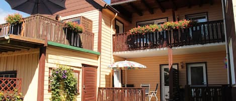 A two-story building with balconies, a wooden deck, and potted plants.