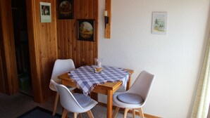 A dining area with a wooden table and two chairs, a checkered tablecloth, and framed pictures on the wall.