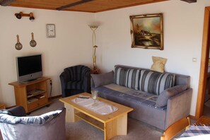 A living room with a television, sofa, armchair, wooden coffee table, and a painting on the wall. - Vacation apartment Bianca - House Reese (Clausthal-Zellerfeld)