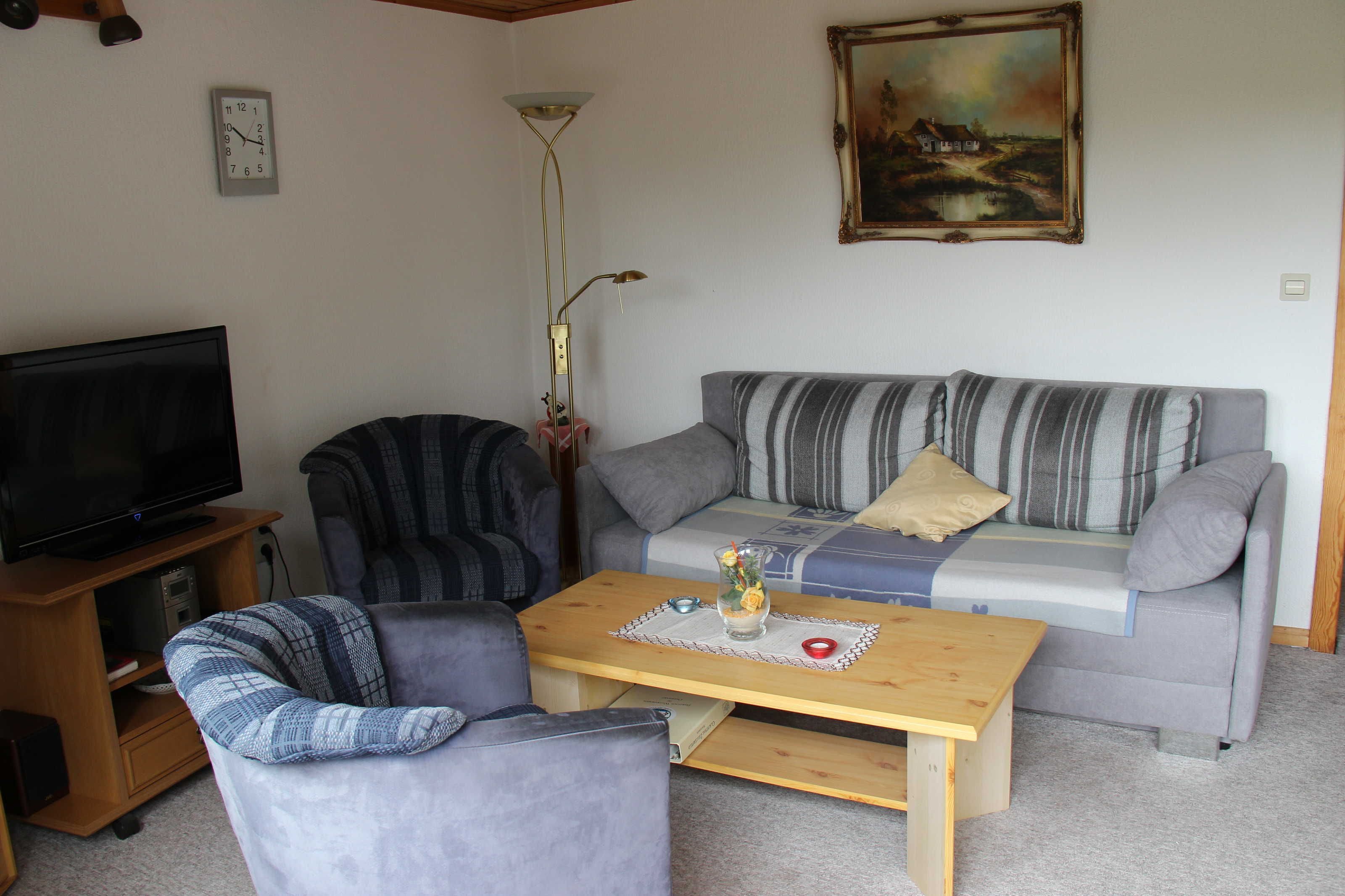 A living room with a sofa, armchair, TV, wooden coffee table, and a painting on the wall.