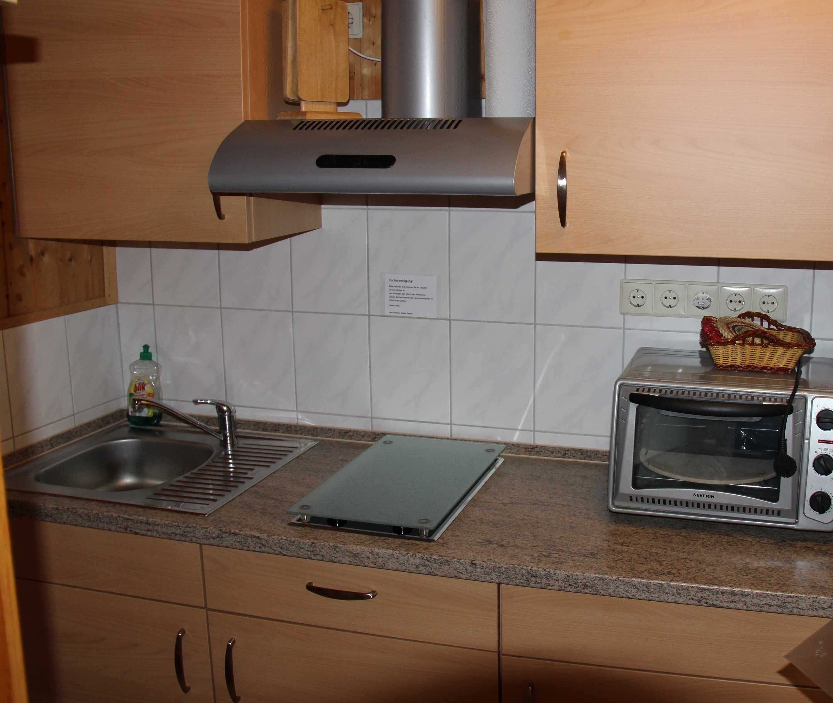 A kitchen with a stainless steel range hood, a toaster oven, a sink, and a small basket on the counter.