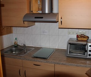 A kitchen with a stainless steel range hood, a toaster oven, a sink, and a small basket on the counter.