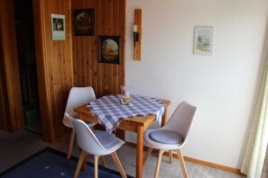 A dining area with a wooden table and two chairs, a checkered tablecloth, and framed pictures on the wall.