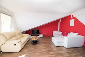 A modern living room with a sloped ceiling, a beige sofa, a white sofa, and a small wooden coffee table.