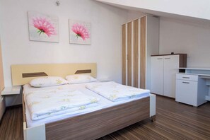 A hotel room with a bed, a desk, and two floral artwork pieces on the wall.