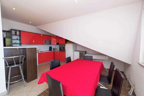 A modern kitchen with red cabinets, a dining area with a red table, and a small kitchenette.