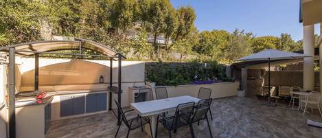Un patio al aire libre con mesa y sillas, una parrilla y una zona de estar cubierta.