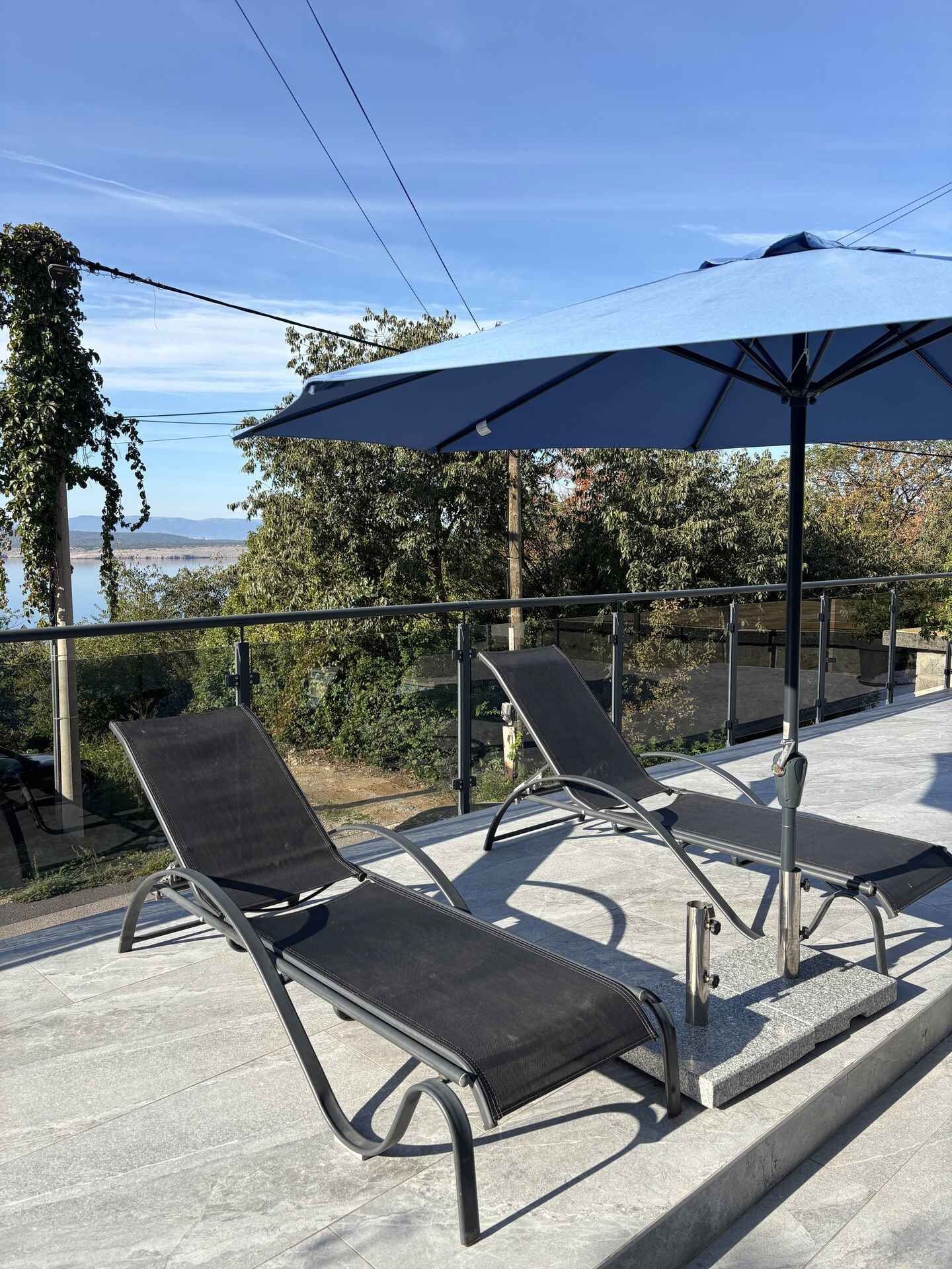 Two lounge chairs with a large umbrella, a concrete floor, and a view of a body of water.