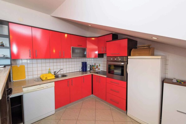 A compact kitchen with red cabinets, a stainless steel oven, and a white refrigerator.