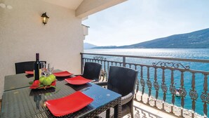 Una mesa de comedor con platos rojos y una botella de vino, ubicada en un balcón con vista a un lago y montañas.
