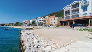 Un pueblo costero con muelles de piedra, diversos edificios que incluyen un hotel con balcones, y un mar azul cristalino.