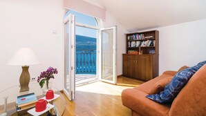 Sala de estar con sofá, una mesa de centro, lámpara, estantería y vista al mar a través de una puerta abierta.