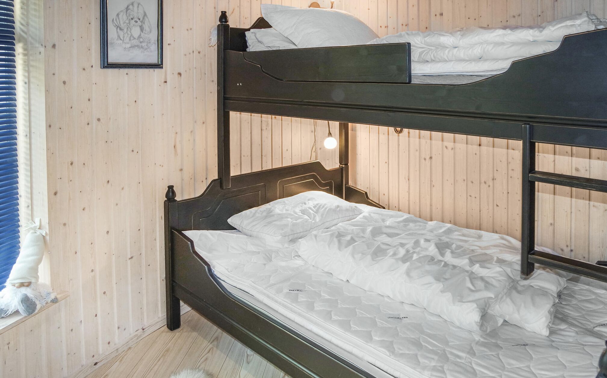 Uma cama beliche com roupa de cama branca em um quarto com paredes de madeira e uma janela com persianas.
