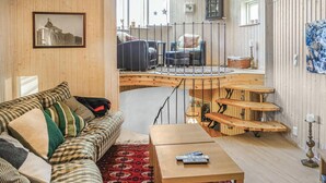 Een gezellige woonkamer met een bank, een bijzettafeltje en een houten trap naar een balkon.