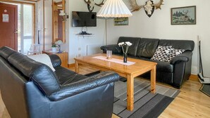 A living room with a black leather sofa, a wooden coffee table, and a black and white patterned rug. There is a television mounted on the wall and a framed picture above the sofa. - 2 bedroom awesome home in Svanskog (Svanskog)