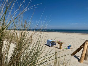 Eine Strandansicht mit Tisch und Stühlen, einer Holzkonstruktion und hohem Gras.