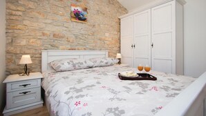 A bedroom with a stone wall, a bed with floral bedding, two bedside tables with lamps, and a wardrobe. - Pet friendly home in Filipana (Filipana)