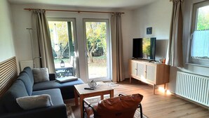 Ein Wohnzimmer mit einer Couch, einem Tisch, einem Fernseher und Blick ins Freie.
