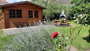 Eine Holzhütte mit Terrasse, umgeben von einem Garten mit Lavendel und einer roten Rose.