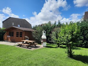 A wooden cabin with a picnic table and a stone sculpture in a garden.