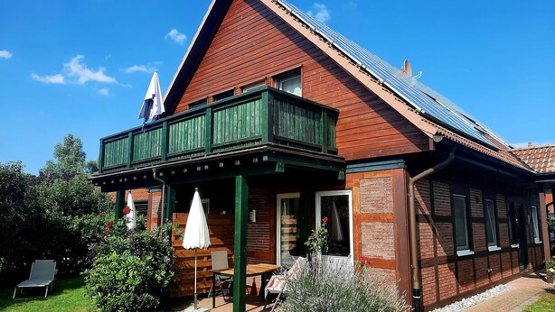 Ein zweistöckiges Holzhaus mit Balkon, Solaranlage und Garten mit Tisch und Stühlen.