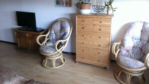 A living room with two wicker chairs, a wooden cabinet, a television, and a decorative poster on the wall. - Vacation apartment 3 for 4 persons - Ferienwohnungen Willrich (Blankenheim)