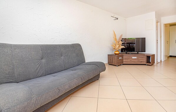 Een moderne woonkamer met een grijze bank, een houten tv-meubel en een vaas met gedroogde planten.
