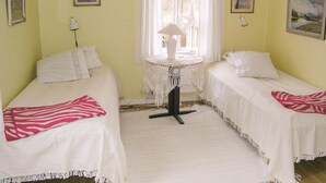 A room with two beds, a small table with a lamp, and a window with curtains.