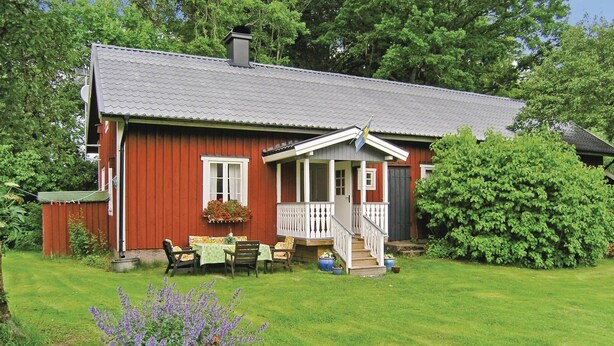 A red wooden house with a porch, a small garden, and a lawn.