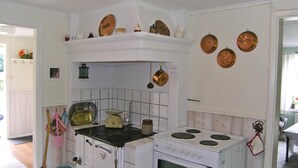 A kitchen with a stove, oven, and various kitchen utensils. There are copper plates on the wall and a lantern hanging above the stove.