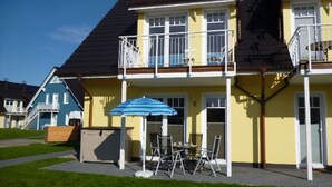 Ein zweistöckiges Haus mit einem Balkon, einer Terrasse und Gartenmöbeln. Auf dem Gebäude ist die Hausnummer 15 sichtbar.