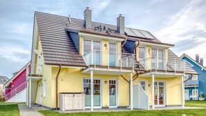 Ein zweistöckiges Haus mit Balkon, überdachter Veranda und gepflasterter Auffahrt.