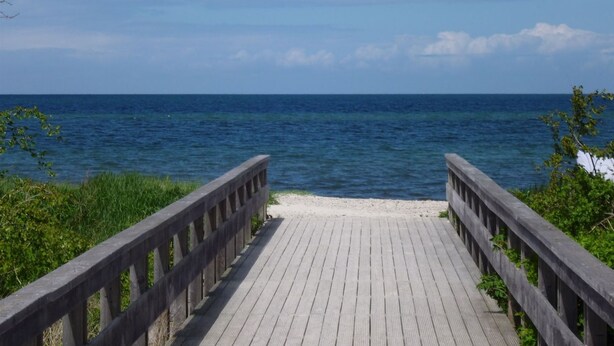 Ein hölzerner Steg führt zu einem Strand mit Blick auf das Meer.
