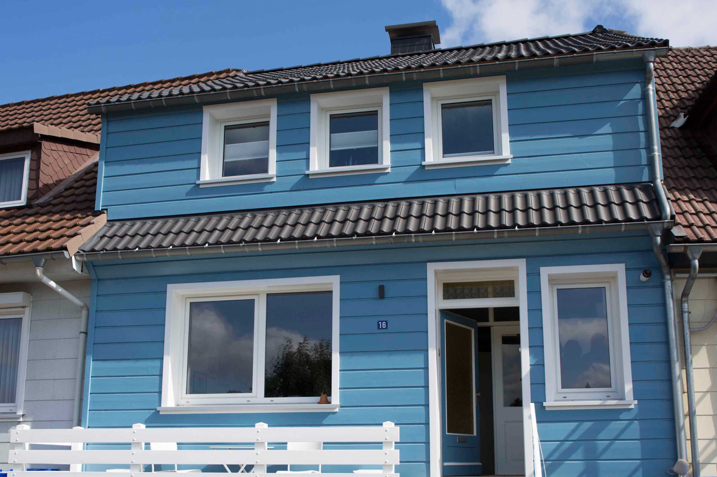 Un bâtiment à deux étages, avec une façade bleue, des encadrements de fenêtres blancs et un toit recouvert de tuiles.