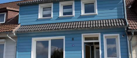 Un bâtiment à deux étages, avec une façade bleue, des encadrements de fenêtres blancs et un toit recouvert de tuiles.